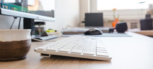 Desktop mit Monitor und kabelloser Tastatur, Maus im Hintergrund